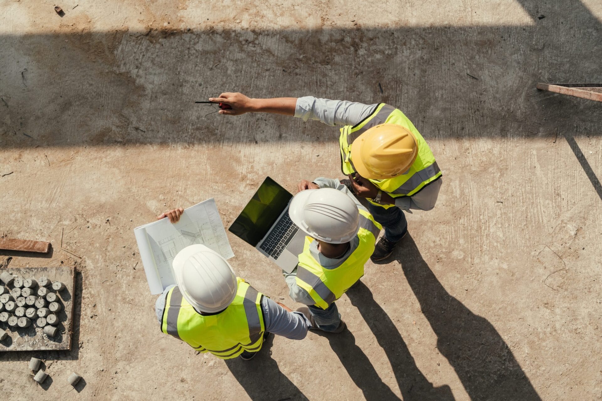Technische Ausarbeitung: Drei Männer mit gelben Westen, stehen im Kreis auf einer Baustelle. 